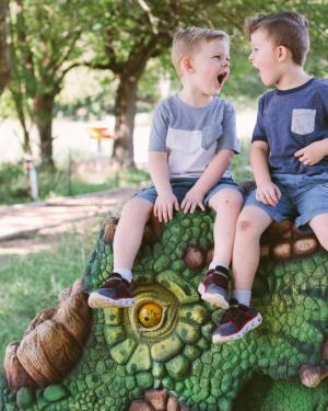 Two boys, roaring while sitting on top of a dinosaur at The Heard