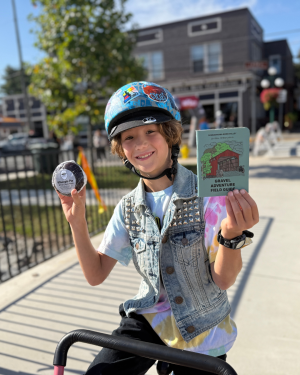 Boy in a blue helmet sits on a bike with a big smile while holding the Susquehanna River Valley Gravel Guide