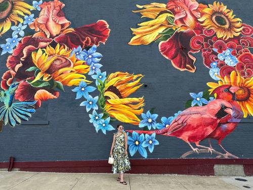 woman standing in front of a vibrant mural with flowers and birds