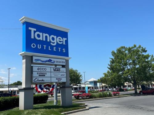 A blue sign with white lettering is shown outside of Tanger Outlets in Rehoboth Beach. The sign lists several stores that are located in the outlets including Vans, Ecco, and Clark's Shoes.