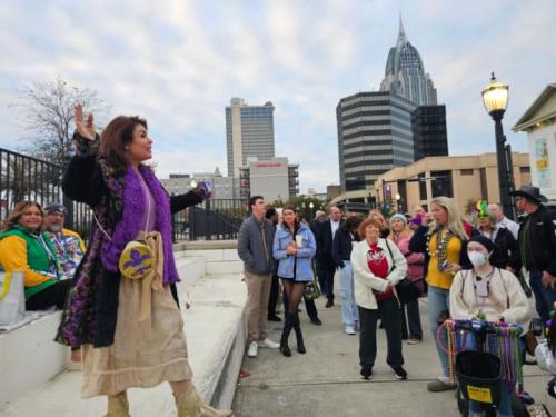 Woman in purple speaks to a group of tourists on a city sidewalk