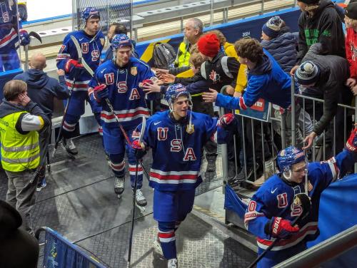 World Juniors hockey tournament showing USA players giving high fives to fans during a break.