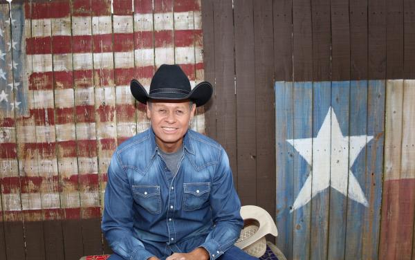 Photo of Neal McCoy in front of fence painting with US and Texas flags