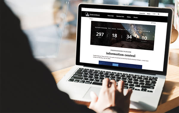 Visit Fredericksburg TX's 2024 lunar eclipse microsite is visible on a laptop screen. It features a countdown to the 2024 lunar eclipse.