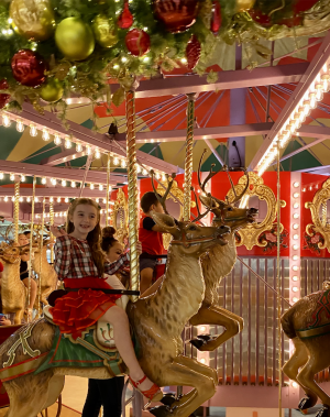 Image of a Christmas-themed carousel with a young child riding on a top of a reindeer.