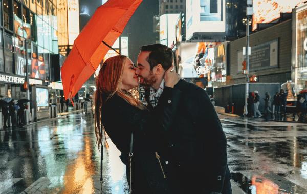 A couple holds an orange umbrella while kissing in Times Square in New York