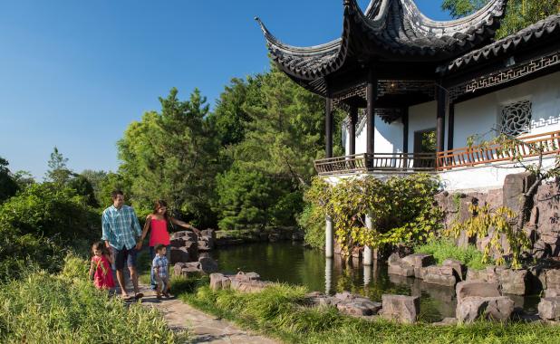 Exterior of a family walking by a building surrounded by green vegetation at the New York Chinese Scholar's Garden at Snug Harbor