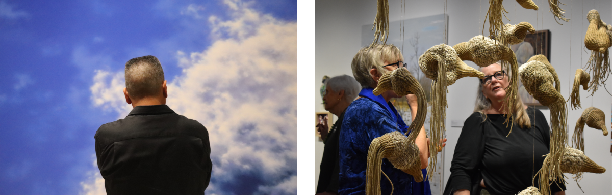 Person standing with their back facing the camera, looking up at a sky painted with white clouds on a blue background at the Muskegon Museum of Art. Two people viewing a hanging art installation featuring several sculpted straw birds at at the Muskegon Museum of Art.