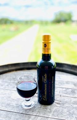 Photo of a bottle of Dominum Tinto Port and Glass on a wine barrel outside of Carter Creek Winery Resort & Spa