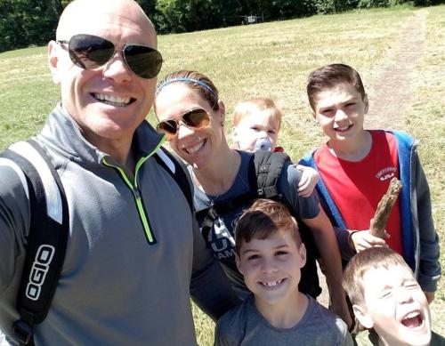dad in sunglasses with mom, three boys and a baby in a backpack on mom's back.