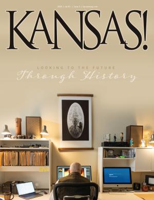 cover of KANSAS! magazine. A man sits at his computer, facing his desk with his back towards the camera