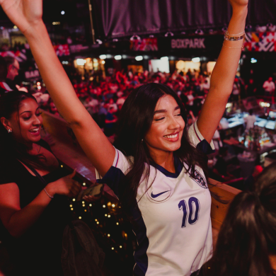 Girl in a football top stood up celebrating.