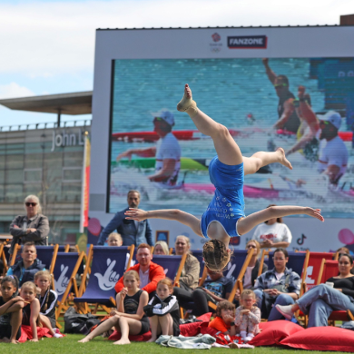 People sat in lounge chairs in Chavasse Park watching a young girl do a back handspring.