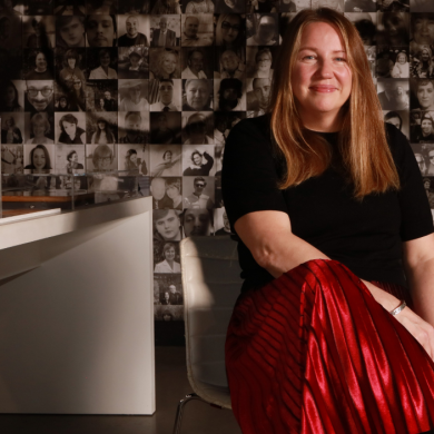 An image of a woman sitting on a chair with her leg crossed, wearing a red skirt and black top.