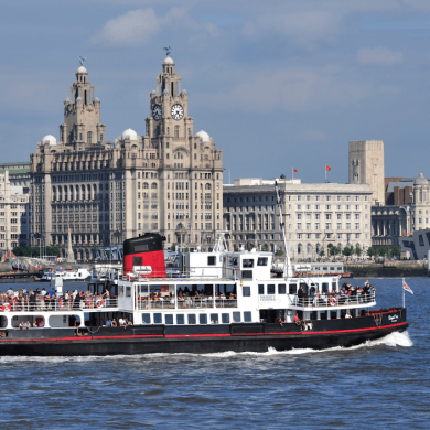 A white ferry on the River Mersey with the Liverpool skyline in the background. It features the Royal Liver Building, The Cunard Building and the Port of Liverpool building.