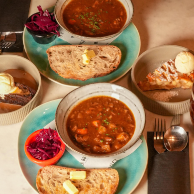 Two bowls of Scouse with crusty bread, a glass of wine and a pint of beer.
