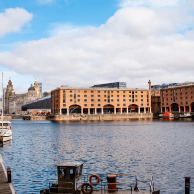 A large group of warehouse brick buildings with a dock of water in the middle of them. There are orange pillars to the left side of the buildings.