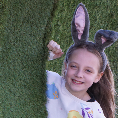 A young child looking at the camera wearing bunny ears and smiling brightly.