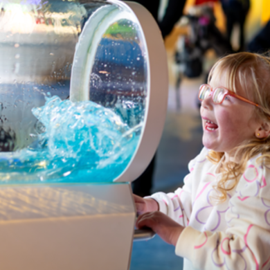 A young child looking at an installation which is a tube with water flowing inside.