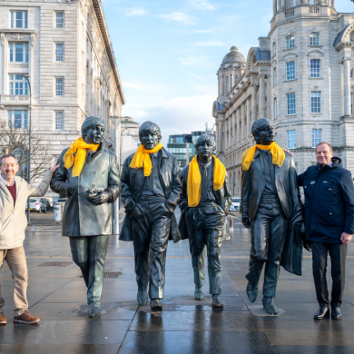 The Beatles Statue with yellow scarves around their necks and two people stood either side.