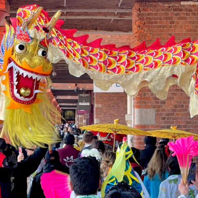 A red and gold dragon being paraded through the Royal Albert Docks with people standing looking.