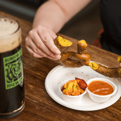 A table with a pretzel and a pint of beer.