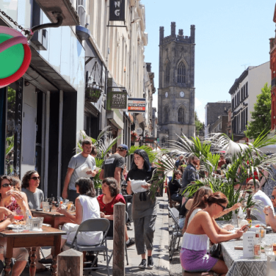 A busy street in Liverpool called Bold Street with people sitting on tables and chairs on the street.