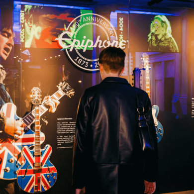 A person stood with their back to the camera looking at a display of guitars in a glass case.