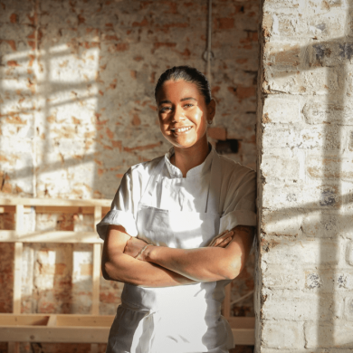Livia Alacron, a chef from Liverpool, wearing a chef uniform leaning against a brick wall.