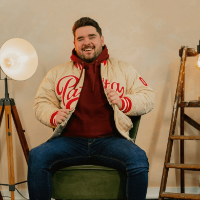 A person sitting on a chair wearing jeans and a cream coloured jacket with lights next to them.