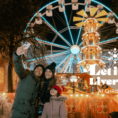 A family taking a selfie style image with a ferries wheel and St George's Hall behind them.