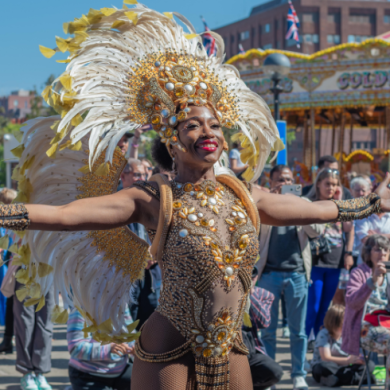 A woman wearing a feather headdress with a jewelled dress and a carousel behind her.
