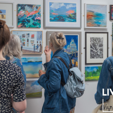 A group of people standing looking at artwork on white walls. There's a logo on the bottom right corner of the image which says 'Liverpool Art Fair'.