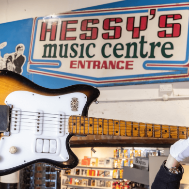 George Harrison's guitar being held up in the air in front of a sign that says 'Hessy's music centre'