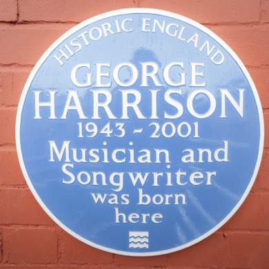 A blue plaque with George Harrison written on it on a wall.