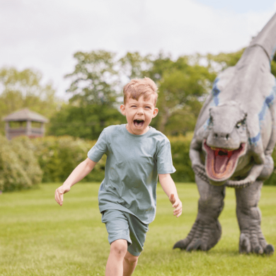 A young boy being chased by a fake dinosaur.