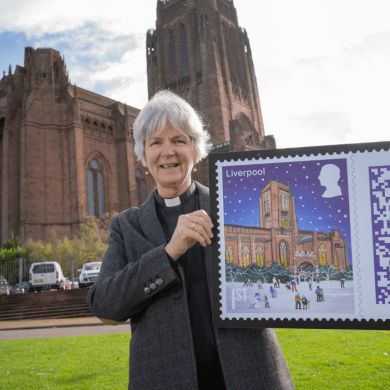 A person holding a large version of the christmas stamp featuring Liverpool cathedral.