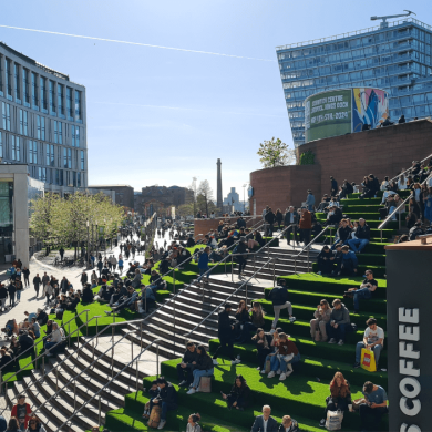 Liverpool one with large steps covered in fake grass with people sitting on them.