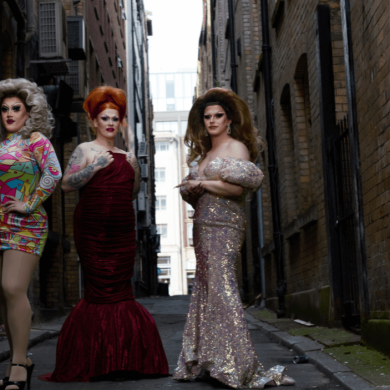 Four people dressed in drag stood in a side street.