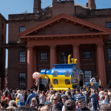 A blue and yellow submarine in a crowd of people at the royal albert dock.