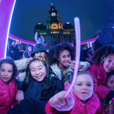 A group of children inside one of the light installations with the royal liver building in the background.