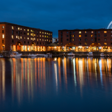 The Royal Albert Dock at night with two large brick warehouse style buildings with lights on in the windows.