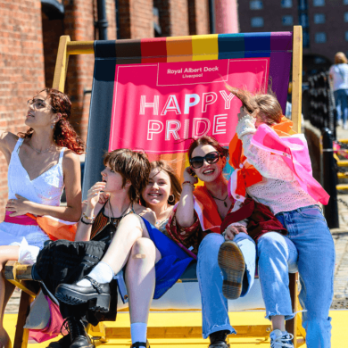 Five people sitting on a large deck chair that says Happy Pride on it.