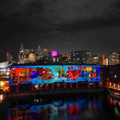 The royal albert dock made up of large warehouse style buildings with a projection shining onto them.