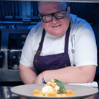 Chef Paul Askew on the pass in a kitchen with a plate of food.