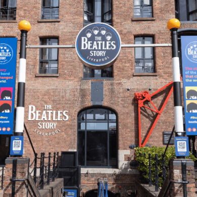 Outside of The Beatles Story with banners of the attraction in blue with the logo hanging above the steps.