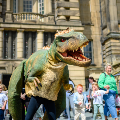 A person dressed up in a dinosaur costume with children and families around them.