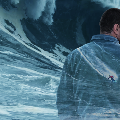A creative double-exposure style image showing a person in a blue jacket viewed from behind, set against a dramatic ocean scene with towering waves. A small surfer is depicted riding a wave within the silhouette of the jacket, blending the person and seascape together. The image uses cool blue tones and textured water effects to create a striking, artistic composition.