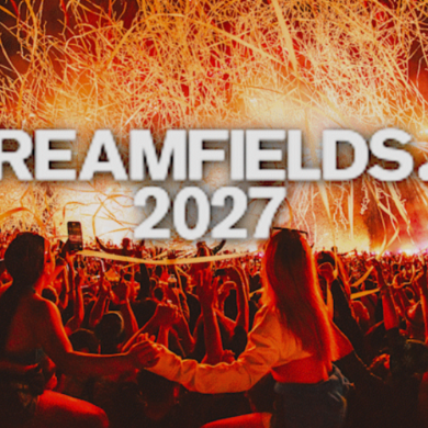 Crowd at a large outdoor music festival illuminated by bright orange stage effects and streamers, with the text “CREAMFIELDS 2027” displayed prominently in the centre. Festivalgoers fill the foreground facing a brightly lit stage amid dramatic pyrotechnics and confetti-like streamers.