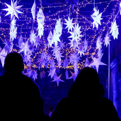 Two people looking at a light display of stars hanging from a ceiling all lit up in blue light.